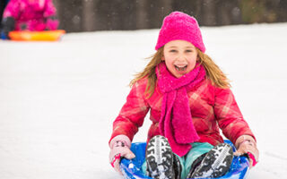 young girl smiling sledding down the sled hill