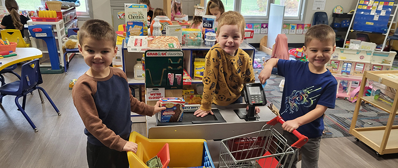 Three boys at Preschool pretending to be a cashier and shoppers.